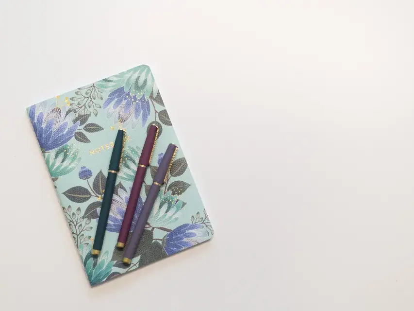 A patterned notebook with two pens on a white table